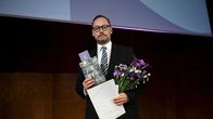 Pavo Teittinen pitelee kädessään kirjaa ja kukkia.
