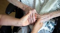 Photo shows a carer and an elderly person holding hands.