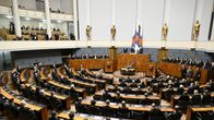 Mustiin pukeutuneet kansanedustajat istuvat eduskunnan istuntosalissa.