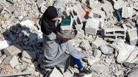 Nainen kerää esineitä Israelin pommittaman rakennuksen raunioista.