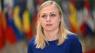 Vaaleahiuksinen nainen sinisessä puserossa, taustalla Euroopan maiden lippuja.