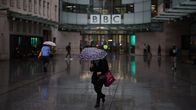  ihmiset kävelevät sateenvarjojen alla BBC:n rakennuksen edessä.