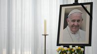 Kynttilä, kukkia ja kehystetty paavi Franciscuksen kuva.