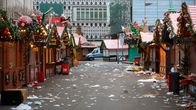 Tomma julmarknadsstånd med skräp spritt över marken efter en marknadskväll, med bakgrund av moderna byggnader.