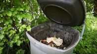 Biojätteen keräysastia  on jätetty auki ulkona pensaiden keskellä.
