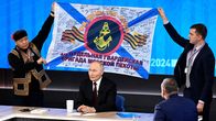 Kaksi henkilöä pitelee laivaston lippua Putinin seläntakana.
