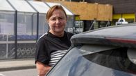 En kvinna med med rödbrunt hår halvt skymd bakom bakdelen av en bil. 