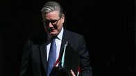 Keir Starmer kaksi mappia kädessään kirkkaassa auringonvalossa puku päällään.