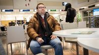 Mies istuu pöydän ääressä aulassa, taustalla palvelupisteitä.