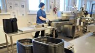 Siniseen suojapukuun pukeutunut nainen pakkaa jälkiruokakiisseliä annosrasioihin .