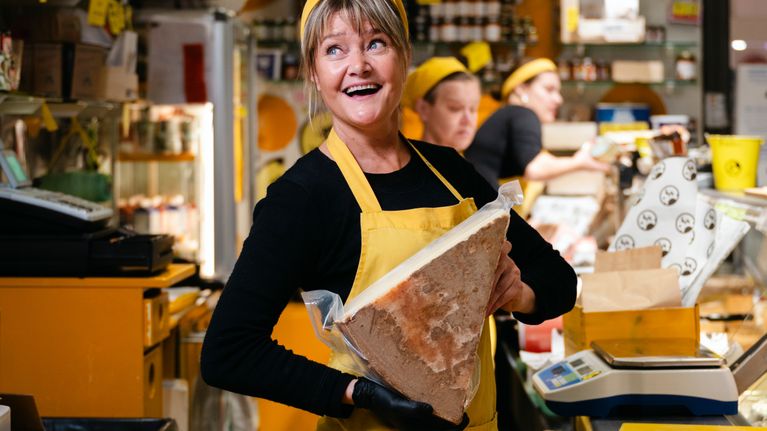 Lentävä lehmä -liikkeen omistaja Laura Mauno pitää sylissään isoa juustokimpaletta ja hymyilee. 