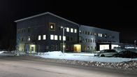 Tumman harmaa kolmikerroksinen kulurakennus talvimaisemassa kuvattuna illalla.