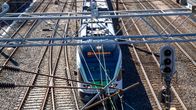 Commuter train and several train tracks alongside it seen from above, with metal frames and wires in the foreground.