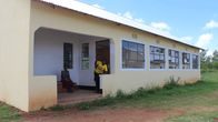 En byggnad i gul, rappad tegel. Vid ingången står och sitter två ungdomar. Det är i Tanzania, Afrika, Ungdomarna är lokala skolelever.