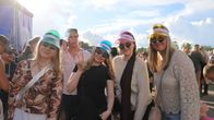 Fyra personer med färgglada solskärmar och solglasögon står utomhus bland andra festivalbesökare.
