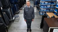Harmaaseen puolustusvoimien asuun pukeutunut Marko Maaluoto seisoo ja katsoo ylöspäin kameraan. Taustalla vaatevarasto, jossa isoja vaatetelineitä.