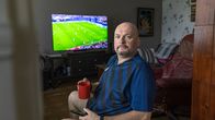 Mies istuu kotona juoden kahvia ja katsoen televisiosta jalkapalloa.