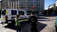 Poliisipakettiauto ajaa aukiolla. Taustalla metroasema ja vaalea kerrostalo. Etualalla kaksi ihmistä.