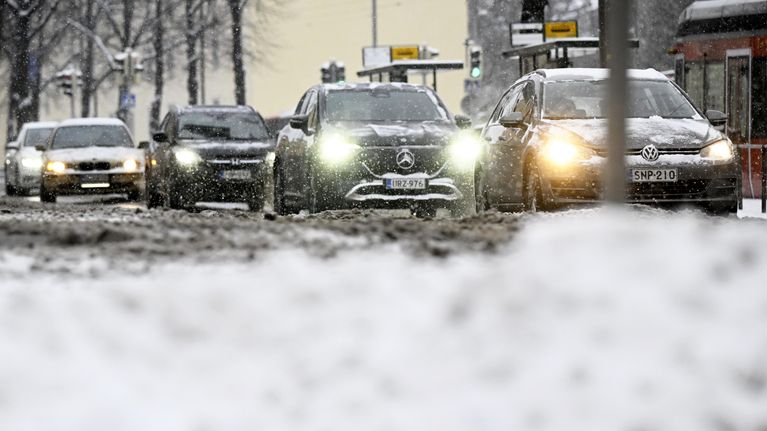 Autoja ajaa lumisateessa Helsingissä, kuvattuna lumikinoksen takaa.