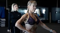 Maarit Tuomi poseeraa kuntosalilla ja valmentaja Marjoriitta Kauppinen opastaa.