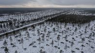 Flygfoto över ett snöklätt landskap med en väg som slingrar sig genom skogen och en elkraftledning som löper parallellt med vägen.