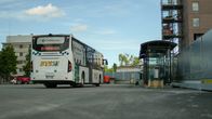En vit buss står vid en busshållplats nära en byggarbetsplats och höghus.