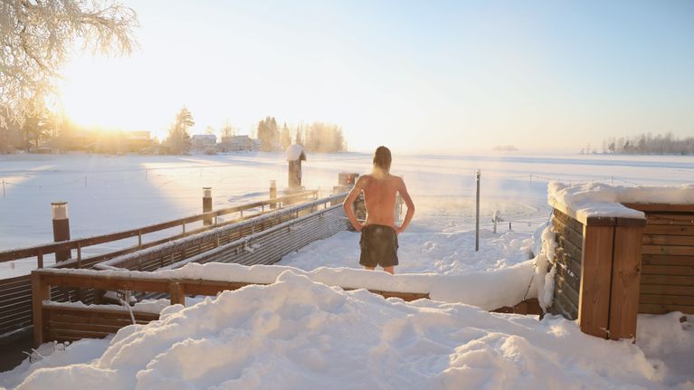 An ice swimmer looks out over a snowy lake on a sunny frosty day.