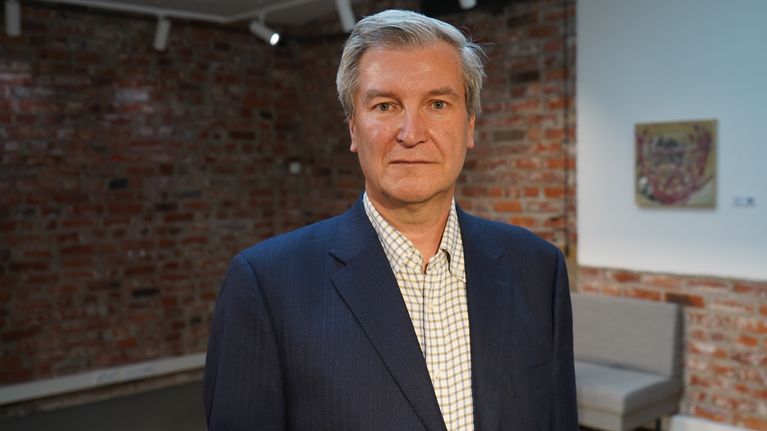 Suurlähettiläs Stefan Lindfors katsoo kameraan vakavalla ilmeellä. Hänellä on harmaat hiukset ja pikkutakki päällään.
