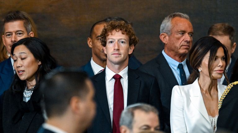 Mark Zuckerberg står mitt i bilden och tittar rakt fram, i en grupp människor. Hans hustru står vänster om honom. 