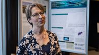 Sari Essayah seisoo symposiumin esittelystandin edessä.
