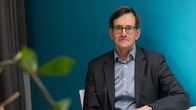 Vesa Vihriälä, istuu pöydän ääressä ja takana sininen seinä.