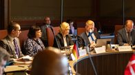 Flera personer sitter runt ett konferensbord med namnbrickor och landsflaggor, inklusive Finlands flagga.