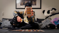 Tunnistamaton nuori nainen istuu sohvallaan ja pitää kasvojensa edessä Tarot-korttia.