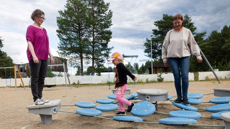 Kaksi naista ja lapsi leikkivät leikkipuistossa tasapainoilulaitteessa Inarin kirkonkylässä.