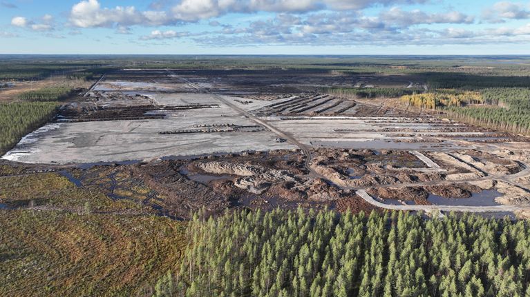 Aerial phot of a large, cleared area of ​​land featuring excavated ditches, damp strips of ground, and surrounding forest.