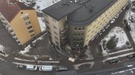 View from above of a snowy street and apartment buildings - one blackened with soot--  with police cars, an ambulance and several people on site,.