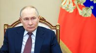 Vladimir Putin istuu puku päällään koristeellisessa tuolissa, taustalla Venäjän federaation presidentin standaari.