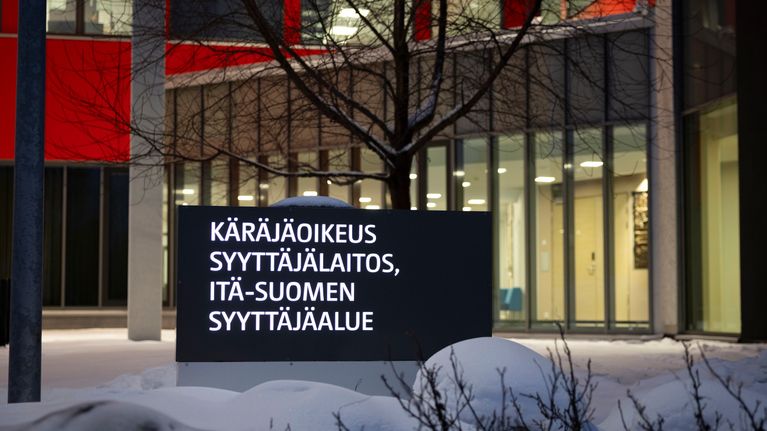 Rakennuksen lumisella pihalla kyltti, jossa tekstit käräjäoikeus, syyttäjälaitos ja Itä-Suomen syyttäjäalue.