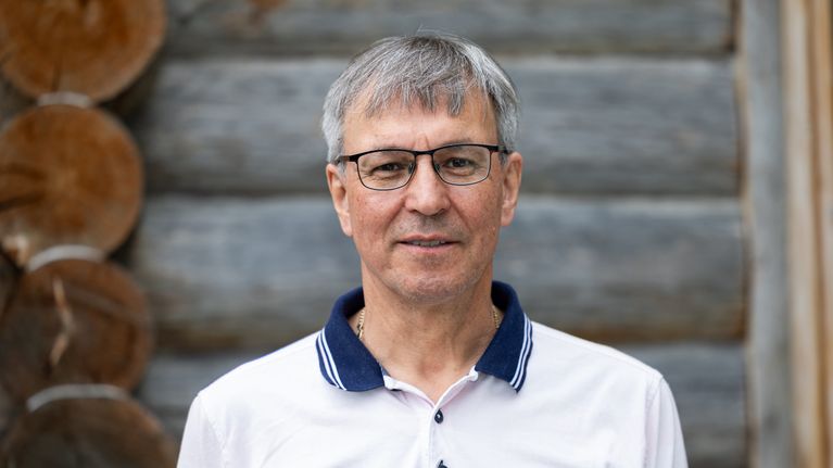 Juha Tapiola lähikuvassa hirsiseinää vasten.