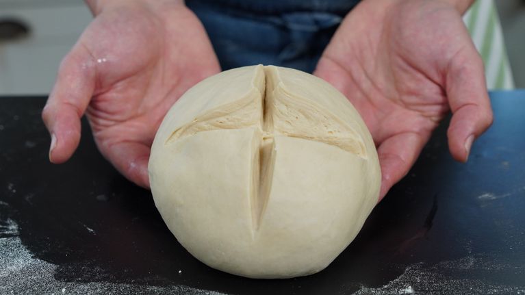 Leipurin kädet pitelevät kauniisti kohonnutta leipätaikinaa, joka on valmiina uuniin paistettavaksi.
