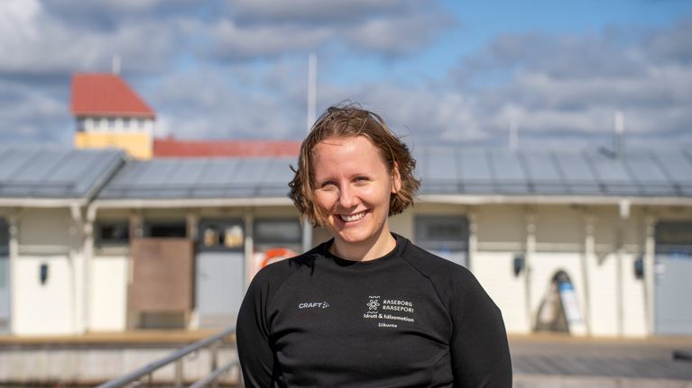 Julia Thurin ler mot kameran med ett vitt hus i bakgrunden.