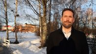 Mustaan takkiin pukeutunut maakunta-analyytikko Jukka Lidman etualalla. Taustalla luminen puisto ja Hämeen punatiilinen linna.