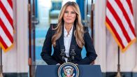Melania Trump puhujankorokkeella, taustalla Yhdysvaltain liput.