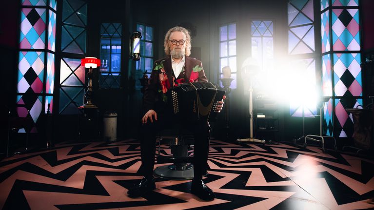 Antti Paalanen UMK26-musiikkivideokuvauksissa. Paalanen istuu parturi-kampaamon tuolissa haitari kädessään.