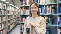 Camilla Nissinen seisoo kirjastossa Rihmasto-teos käsissään.