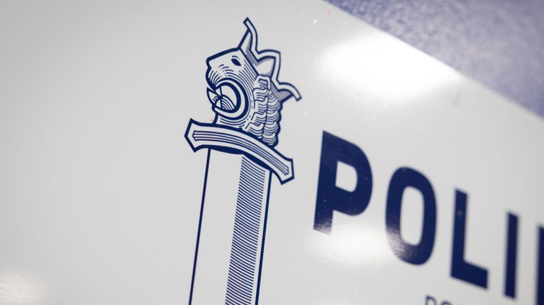 Sinivalkoiset poliisin miekkatunnus ja poliisi-teksti seinän kyltissä.