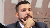 Tobias Rausch istuu pöydän ääressä käsi leuallaan, taustalla seinä ja osittain näkyvää tekstiä.