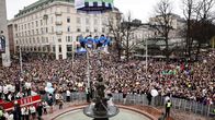 Thousands of people surrounding the Havis Amanda statue on a grey day in downtown Helsinki.