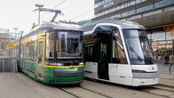 Kaksi raitiovaunua. Toinen on vihreä, toinen valkoinen.