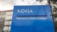 A large blue sign saying Welcome to Nokia Campus, with an office building and trees behind it.